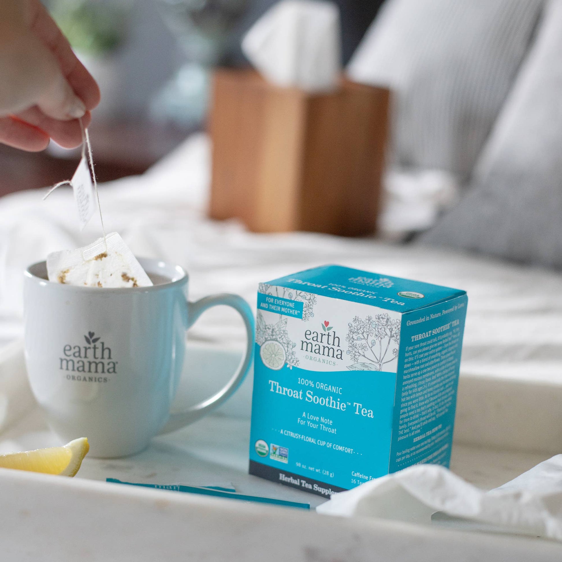 Earth Mama box of Throat Soothe tea with a mug and lemon on a table.