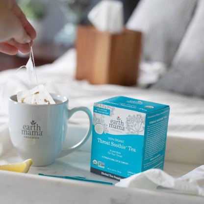 Earth Mama box of Throat Soothe tea with a mug and lemon on a table.