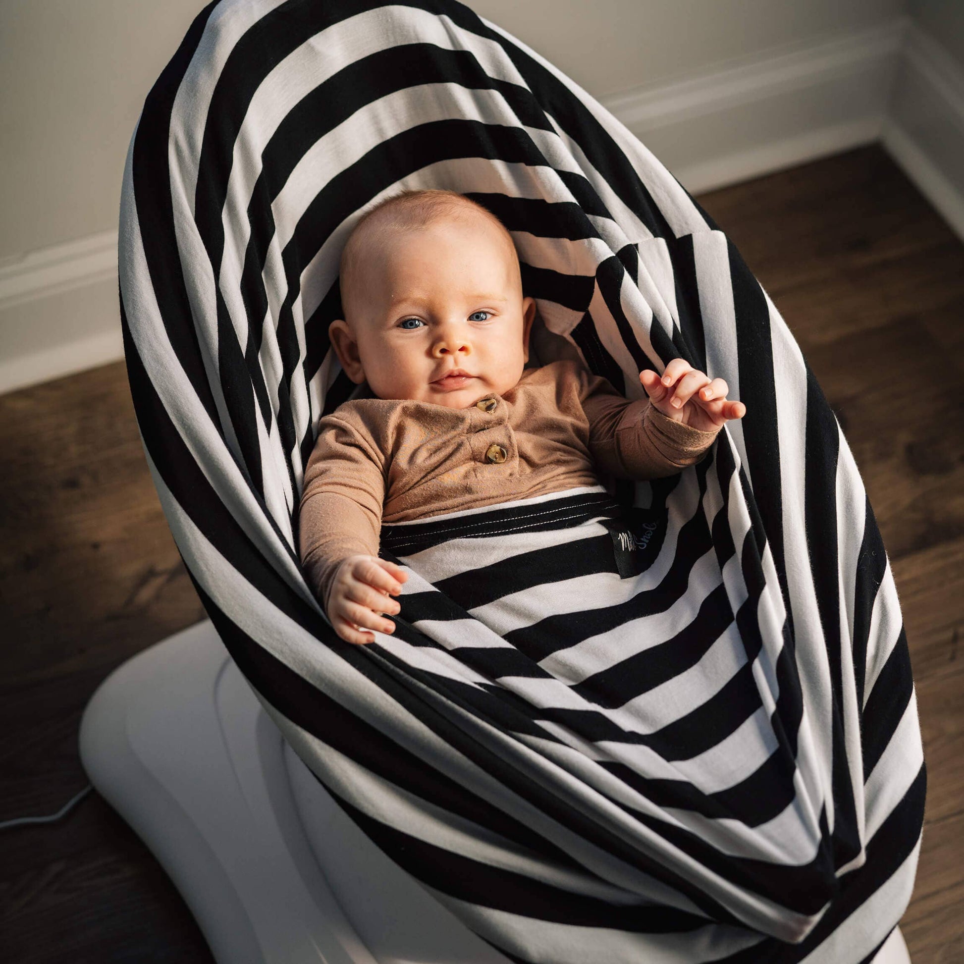 Baby in a baby rocker with a striped cover on a wooden floor