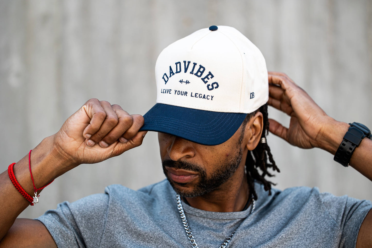 Man wearing a cap with 'DADVIBES' text, adjusting it against a neutral background