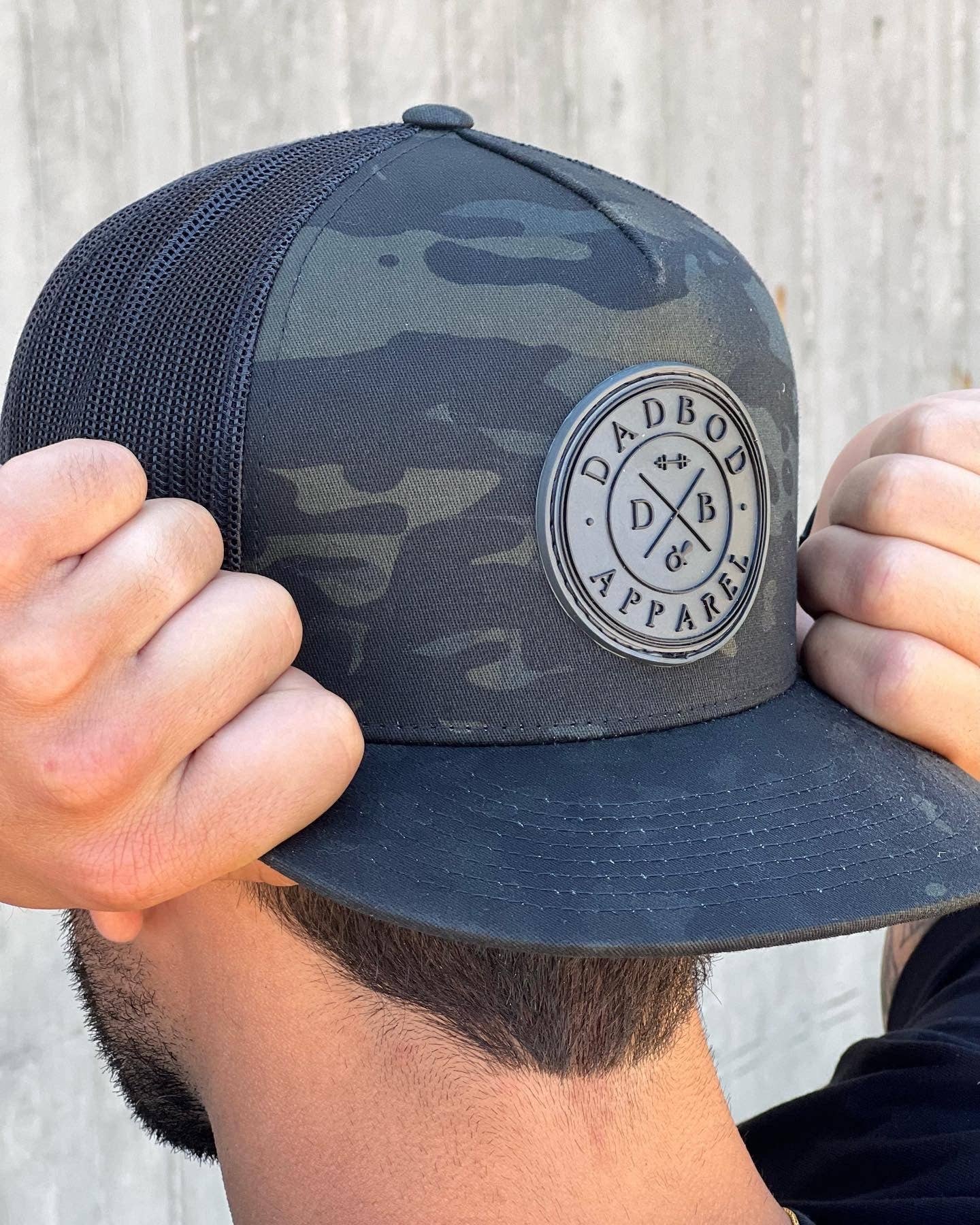 Person adjusting a camouflage cap with a brand logo against a light background