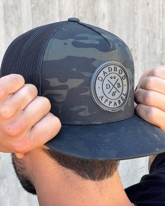 Person adjusting a camouflage cap with a brand logo against a light background