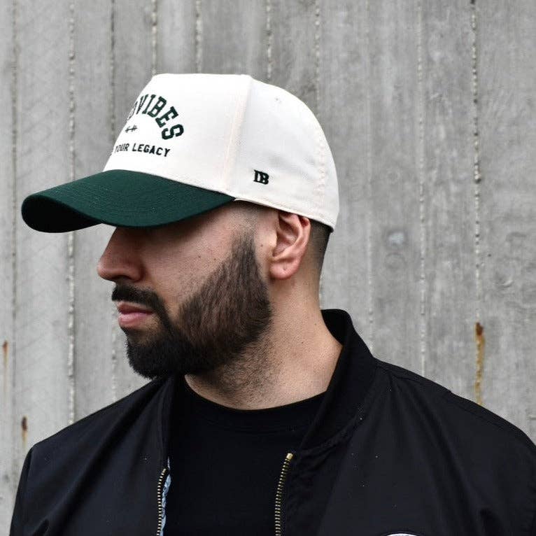 Man wearing a white and green cap with text against a concrete wall.