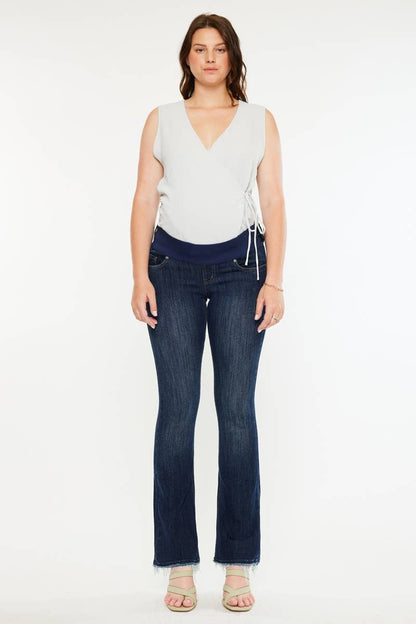 Pregnant woman wearing a white sleeveless top and dark blue jeans on a white background