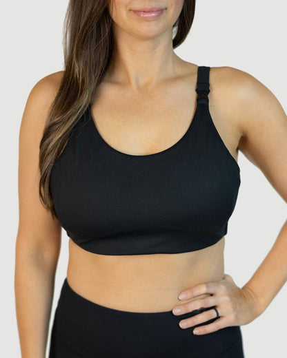 Woman wearing a black sports bra with clip down nursing access and leggings on a plain background