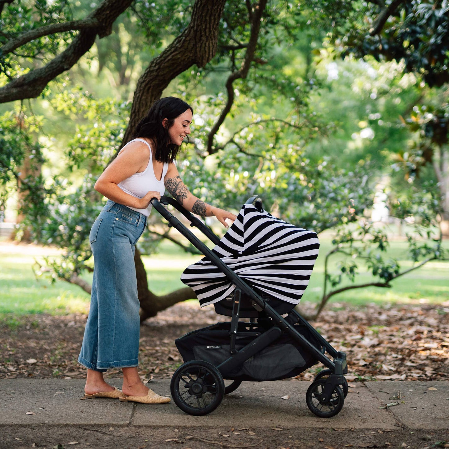 Woman pushing a stroller with a striped cover in a park