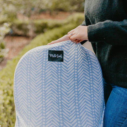 Person holding a car seat with a blue patterned cover and a visible brand label outdoors.
