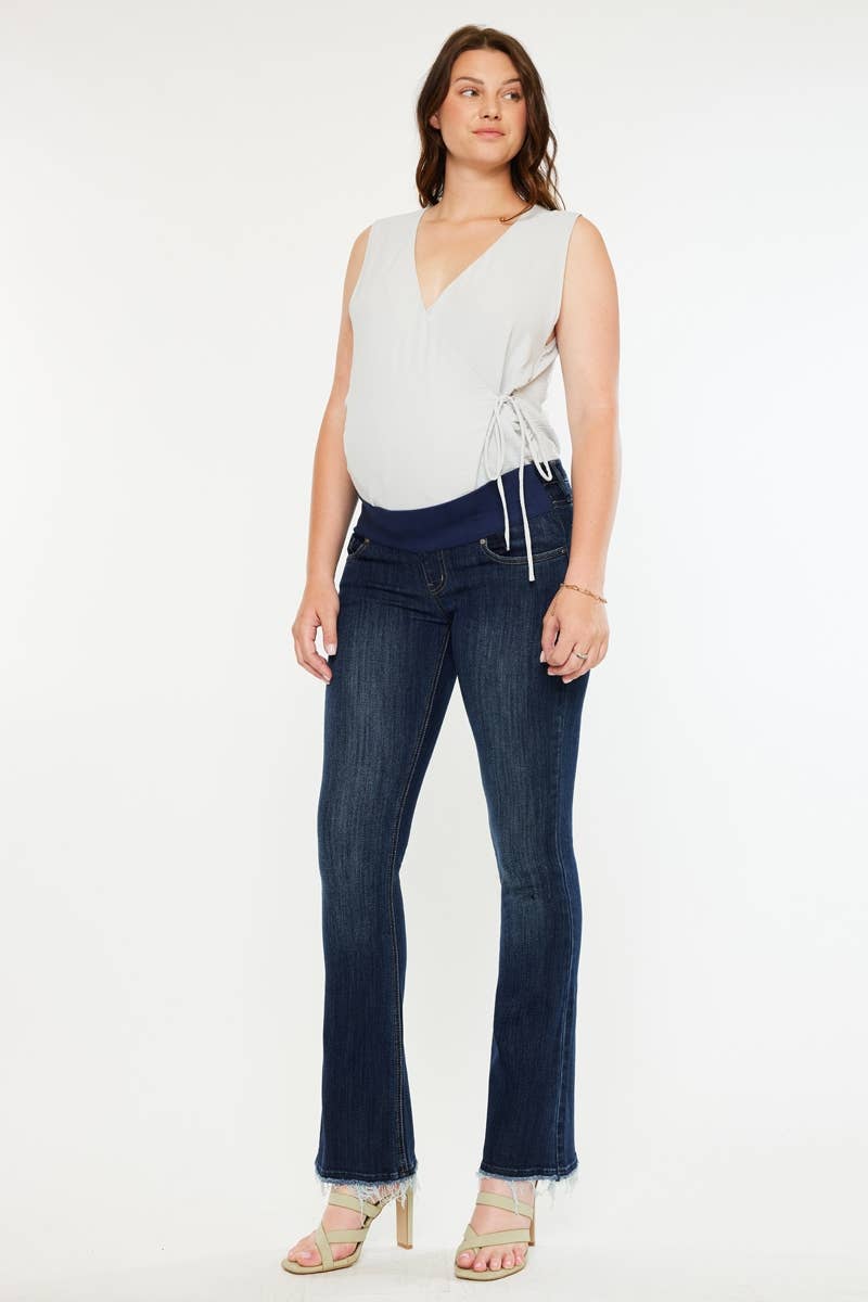 Pregnant woman wearing a white sleeveless top and dark blue jeans on a white background