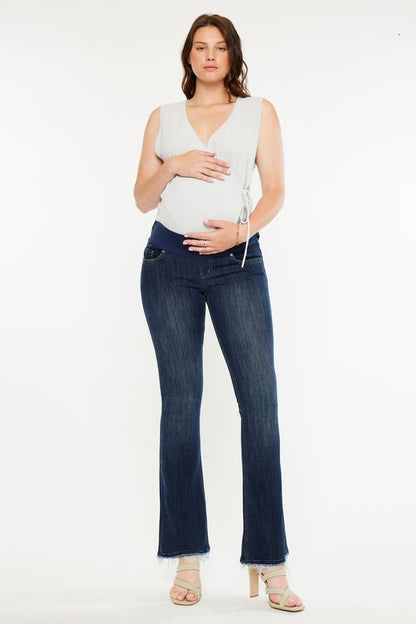 Pregnant woman wearing a white top and dark blue jeans on a white background