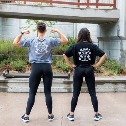 Two people wearing matching t-shirts that say "Moms lifting club" and leggings outdoors.