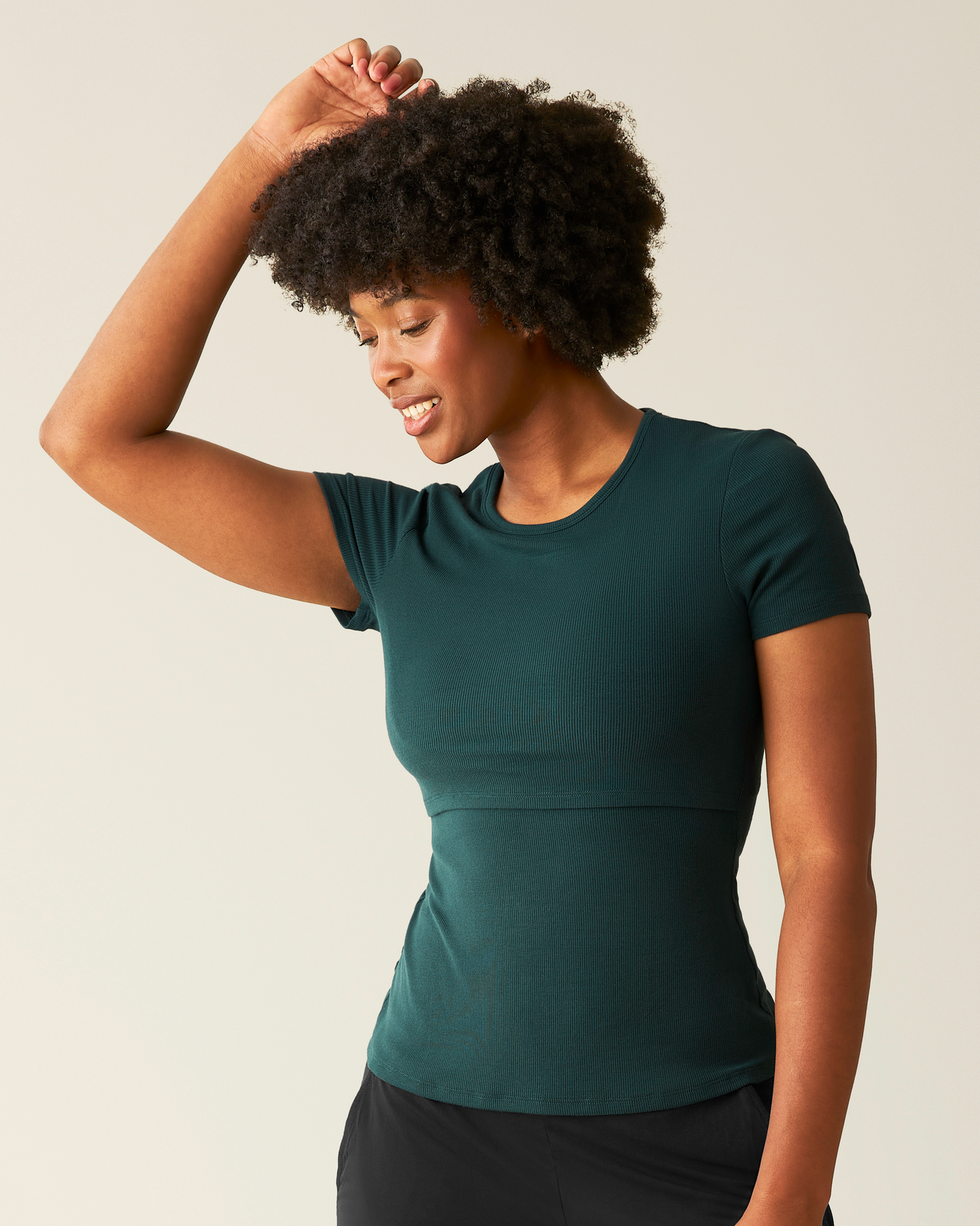 Woman wearing an evergreen ribbed t-shirt with nursing access against a beige background