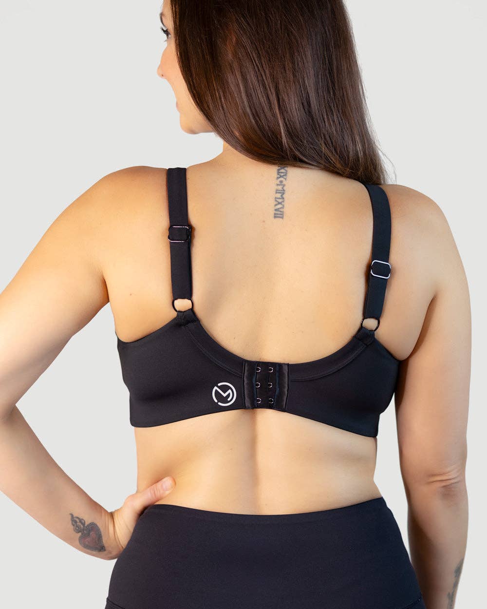 Black sports bra with three-clip back closure worn by a woman on a plain background