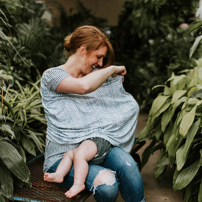 Woman nursing her baby wrapped in a cover amidst green plants