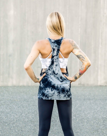 Woman wearing a tie-dye tank top that says "Strong As A Mother" and black leggings with a neutral background