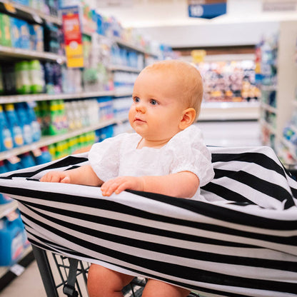 Baby in a cart with a striped cover in a grocery store aisle.