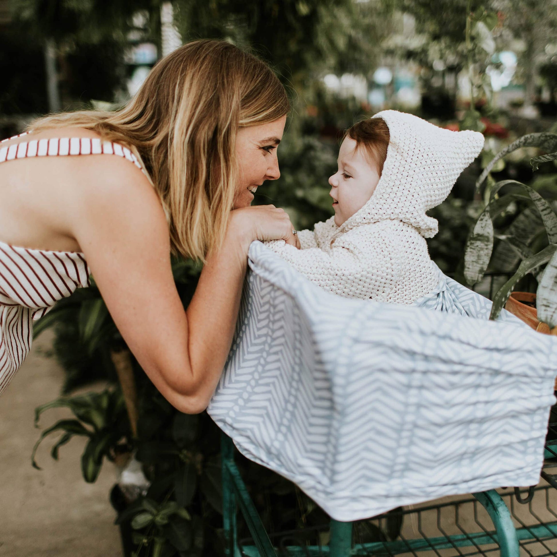 Woman smiling at a baby sitting in a cart with a blue patterned cover