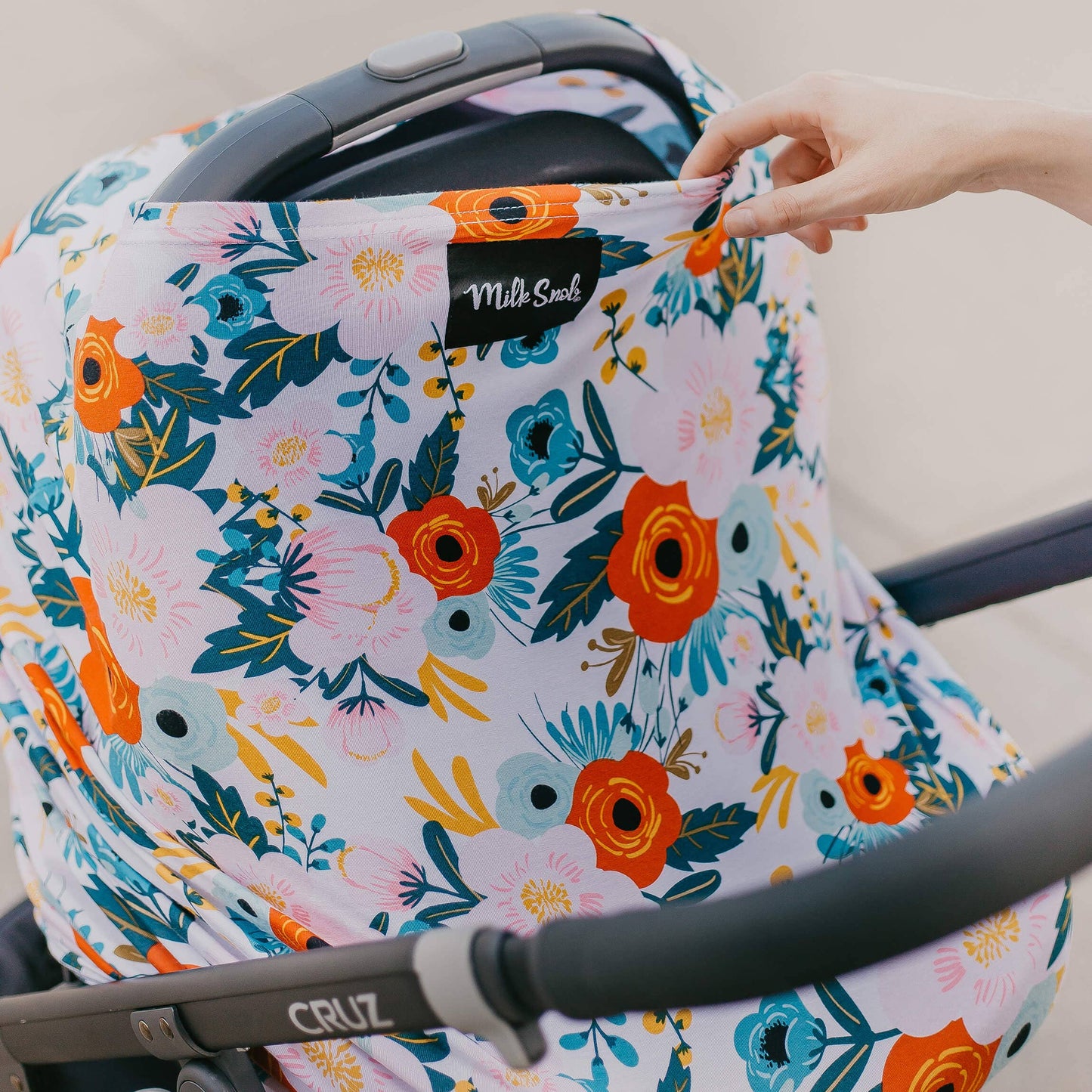 Floral-patterned car seat cover being adjusted on a car seat attached to a stroller.