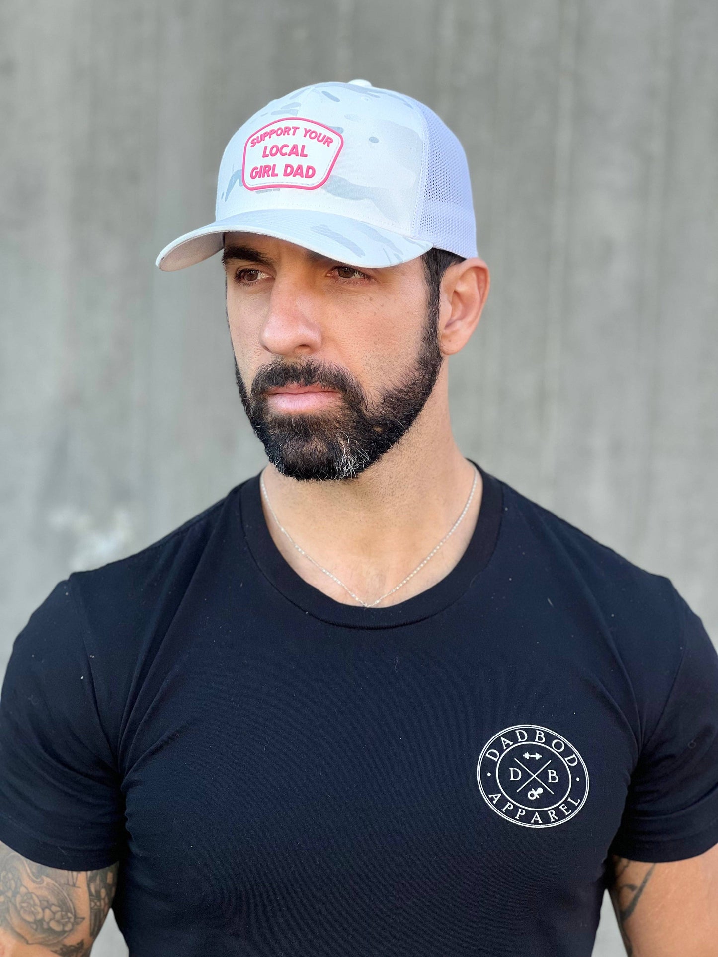 Man wearing a black t-shirt with a logo and a white cap against a gray background