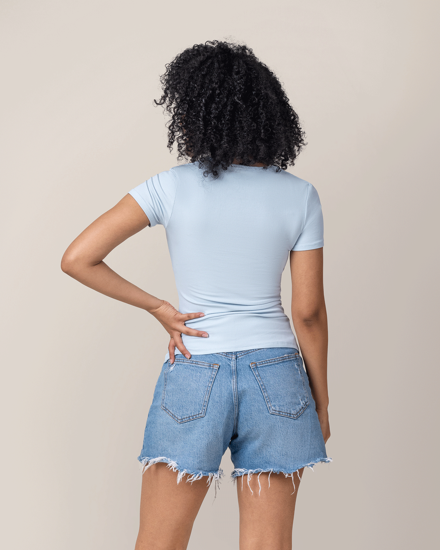 Person wearing a light blue nursing t-shirt and denim shorts against a beige background