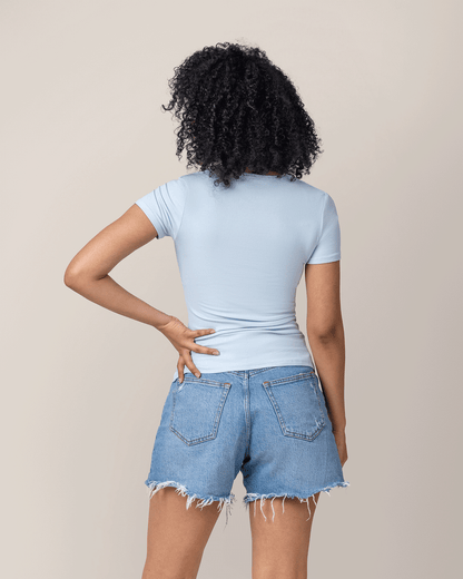 Person wearing a light blue nursing t-shirt and denim shorts against a beige background