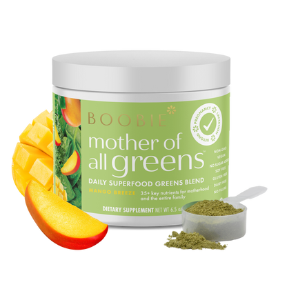A tub of Boobie Superfoods Mother of All Greens powder in the Mango Breeze flavor with a scoop of the powder and a mango next to it.