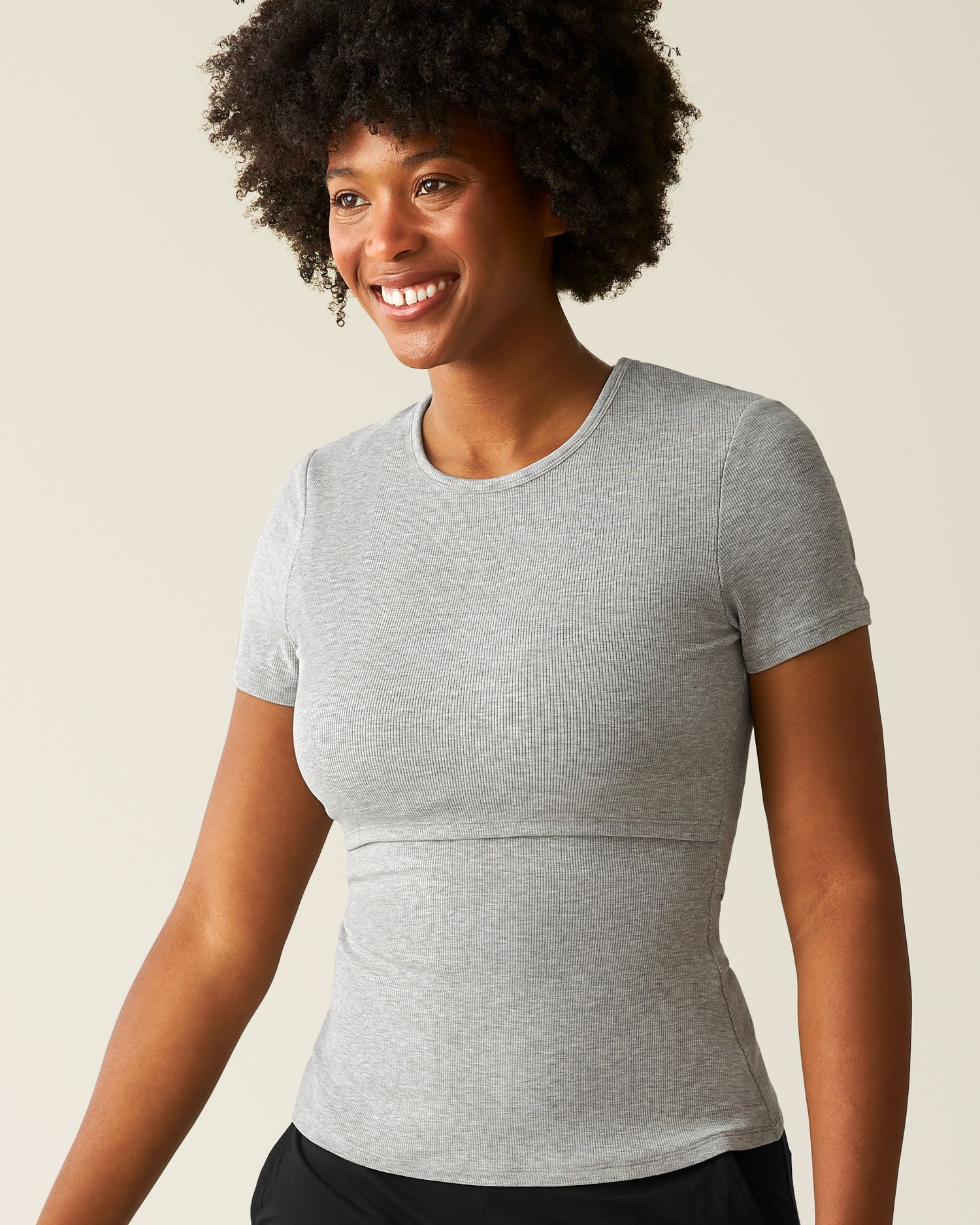 Woman wearing a gray t-shirt with nursing access against a beige background