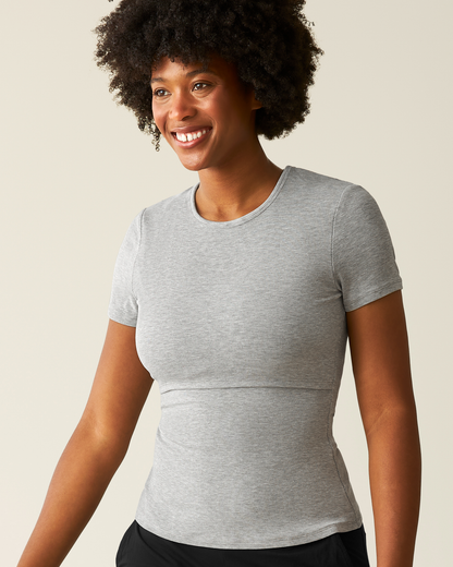 Woman wearing a gray t-shirt with nursing access against a beige background