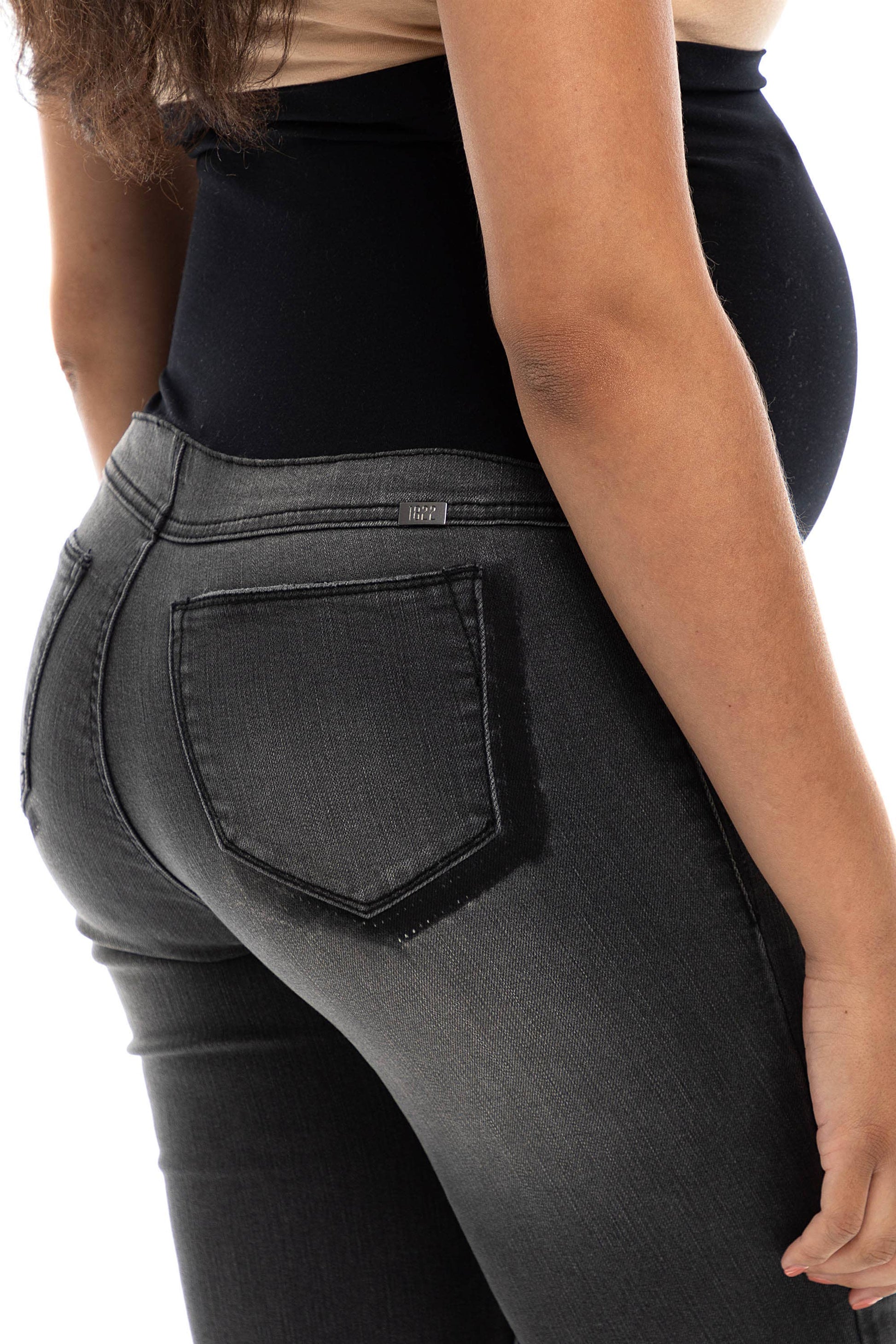 A woman in dark grey, skinny maternity jeans with a bellyband.