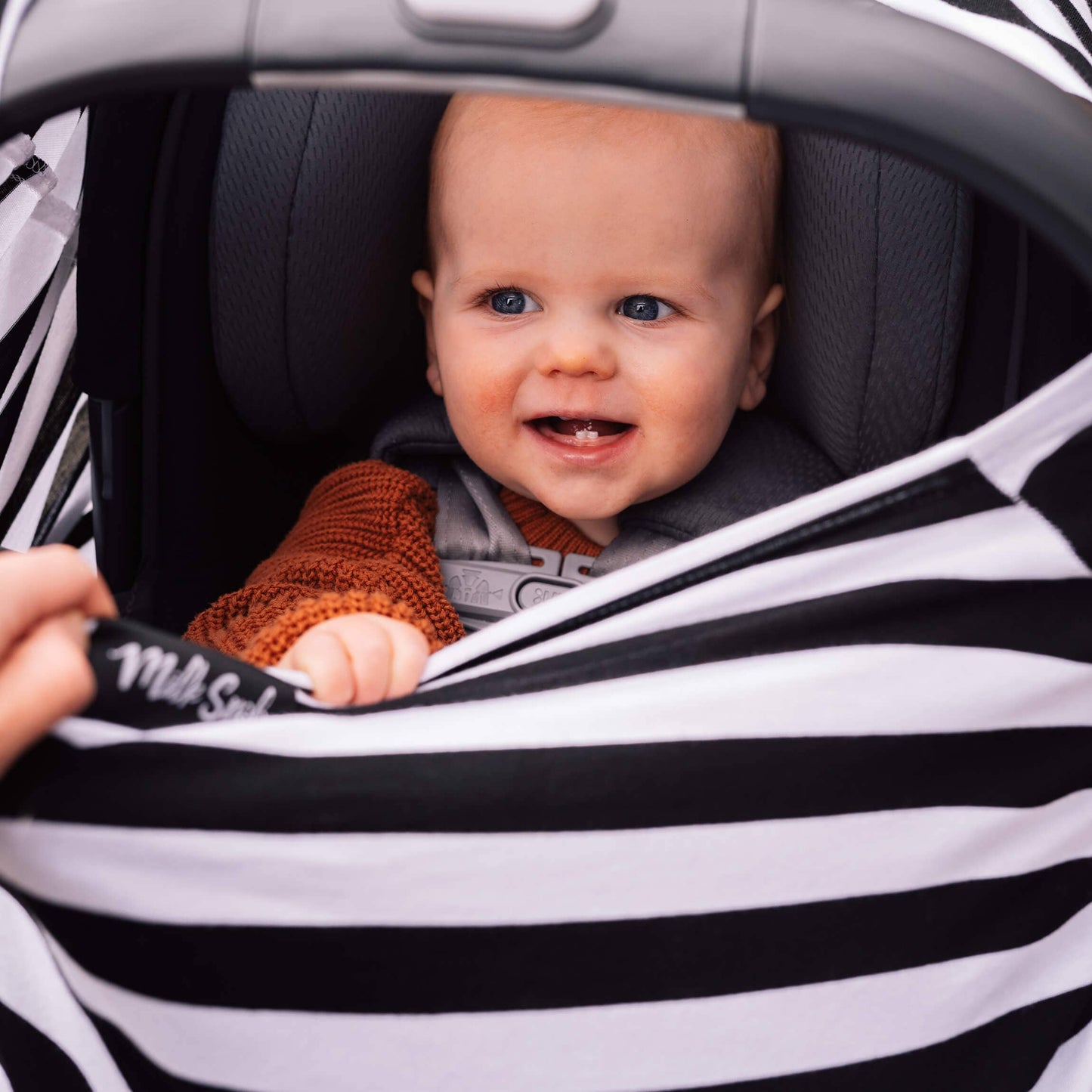 Baby sitting in a car seat with a striped cover, smiling.