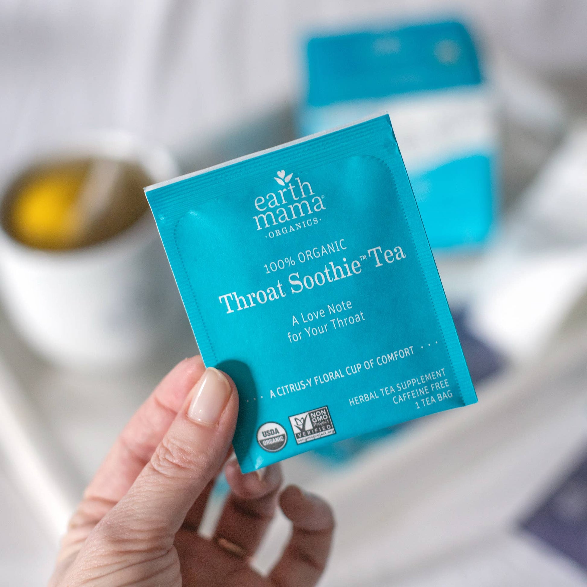 Hand holding an Earth Mama Organics Throat Soothe tea package with a blurred background