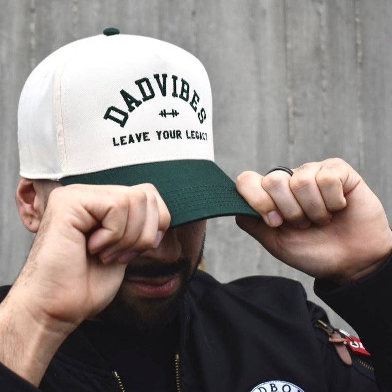 Person wearing a cap with 'DADVIBES LEAVE YOUR LEGACY' text against a gray background