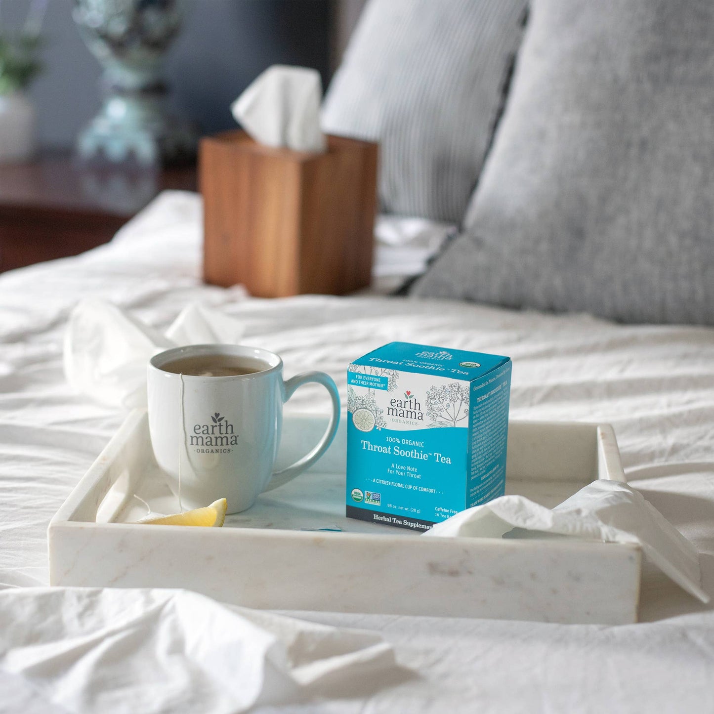 Tray with a mug of tea and a box of Earth Mama Throat Soothe Tea on a bed.