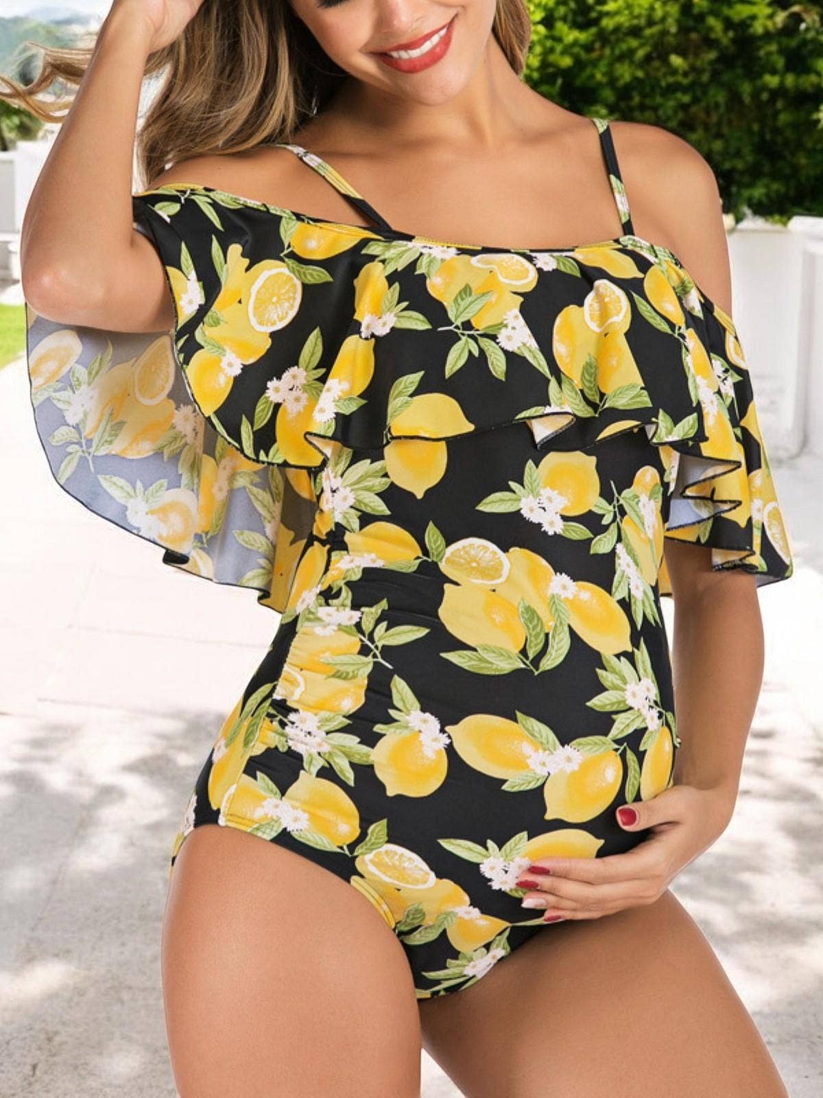 Pregnant woman wearing a black swimsuit with lemon and flower pattern outdoors.
